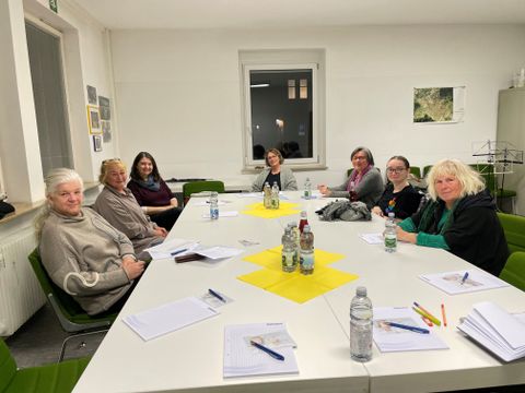 Das Bild zeigt sieben um den Tisch sitzende Frauen, die in eine Richtung blicken.